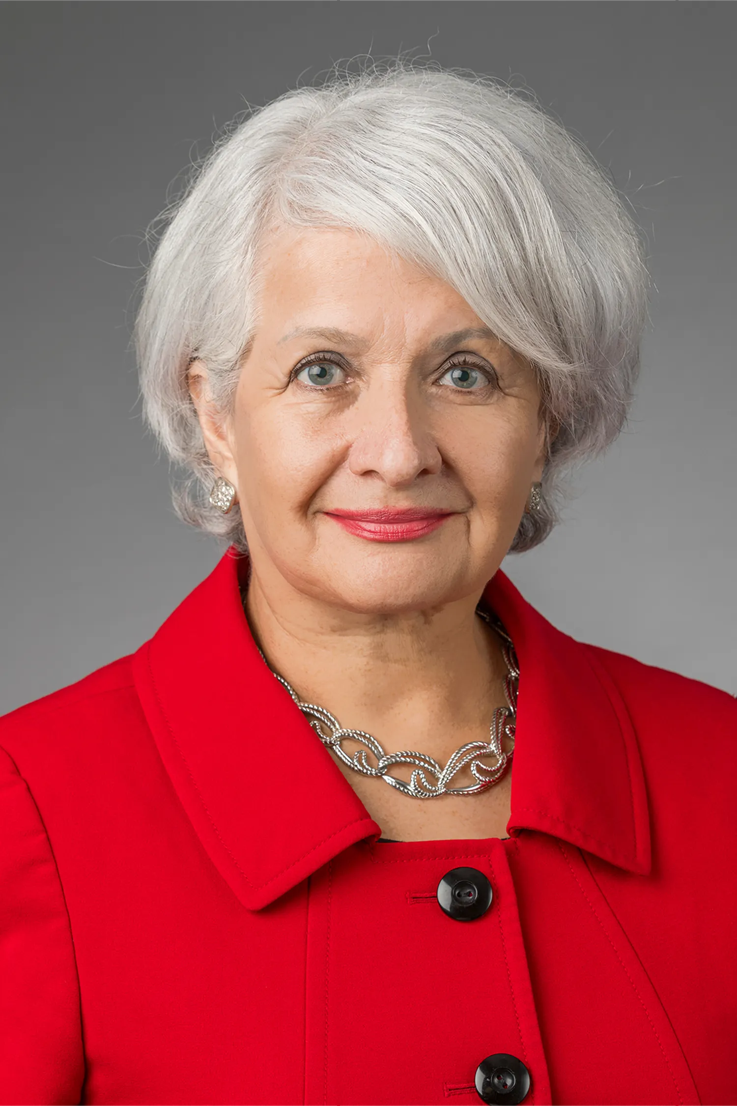Professional headshot of a Hispanic Health Coalition leader with silver hair, wearing a red blazer and pearl necklace.