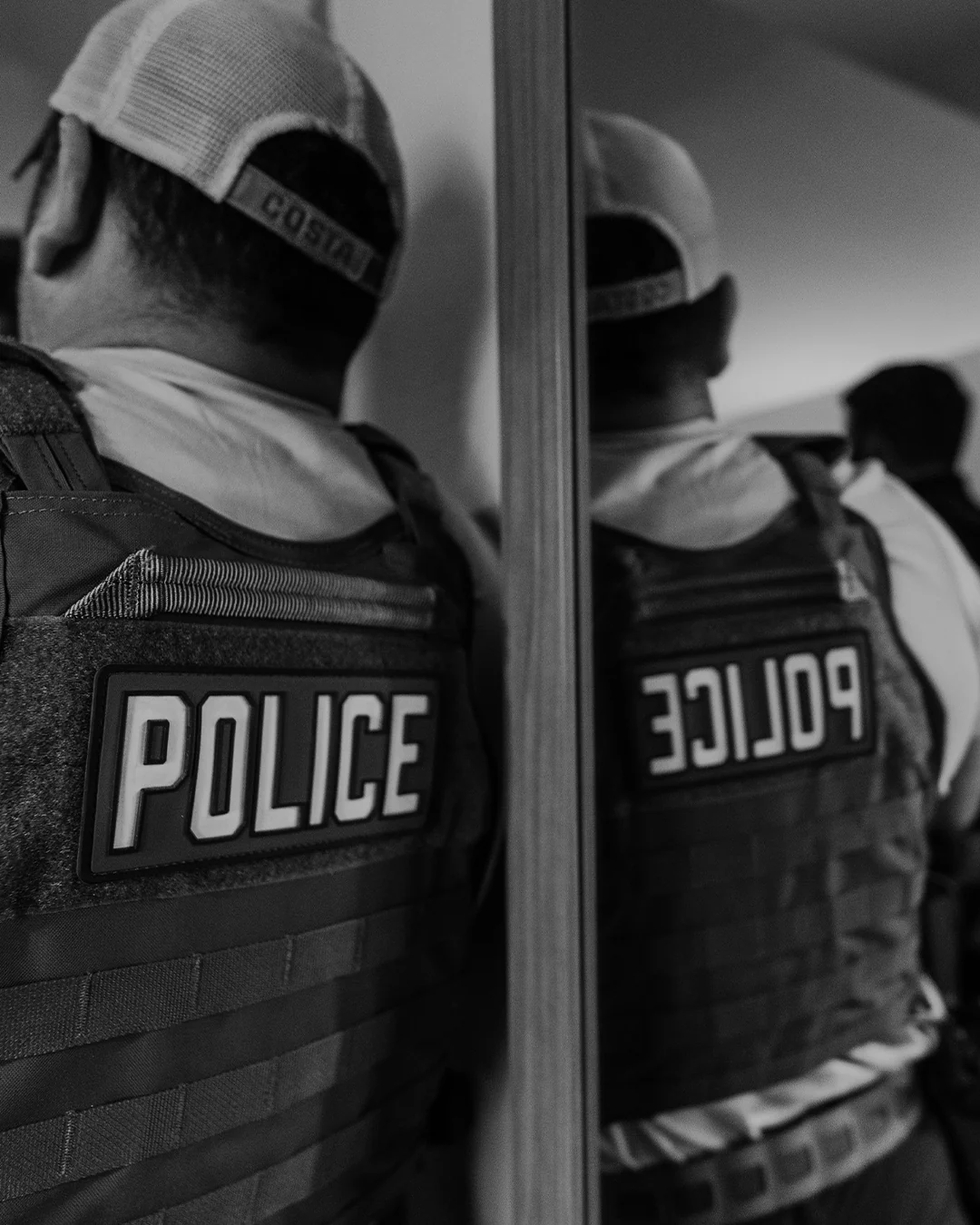 Officer in a police vest during an operation, seen from behind beside a mirror