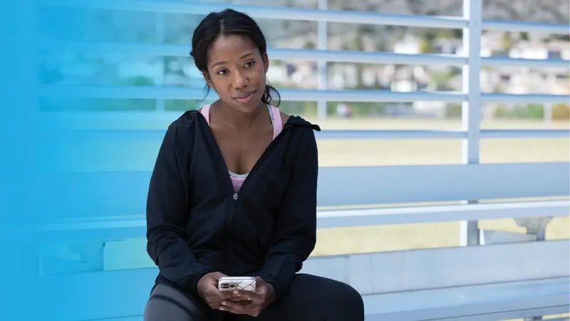 A young woman holding her phone, looking sad