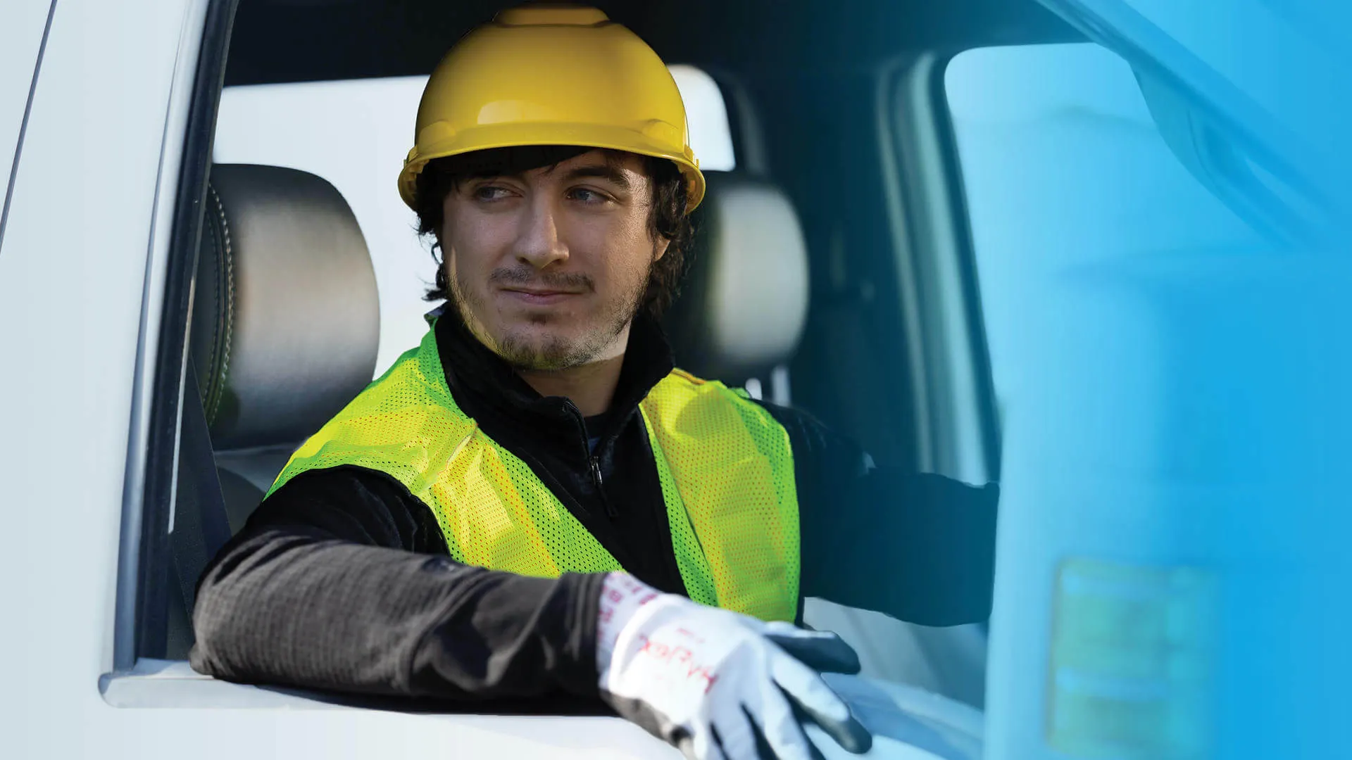 A young man with a hard hat and high visibility vest sitting in a truck, with a wan smile on his face