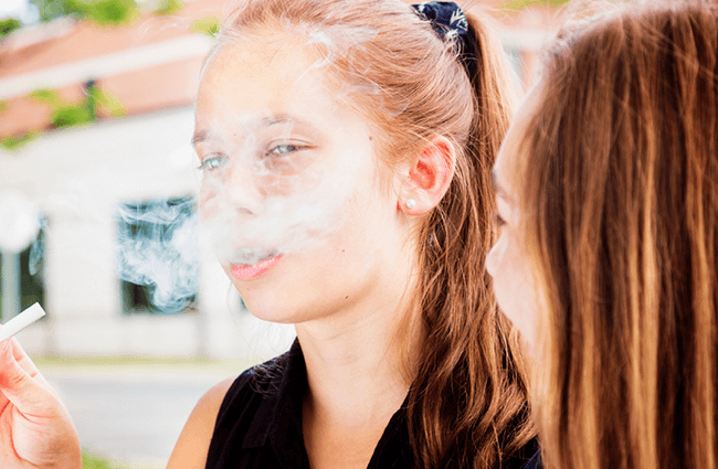 A young teen blowing out smoke