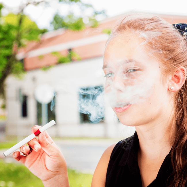 A young teen blowing out smoke from a vaping device