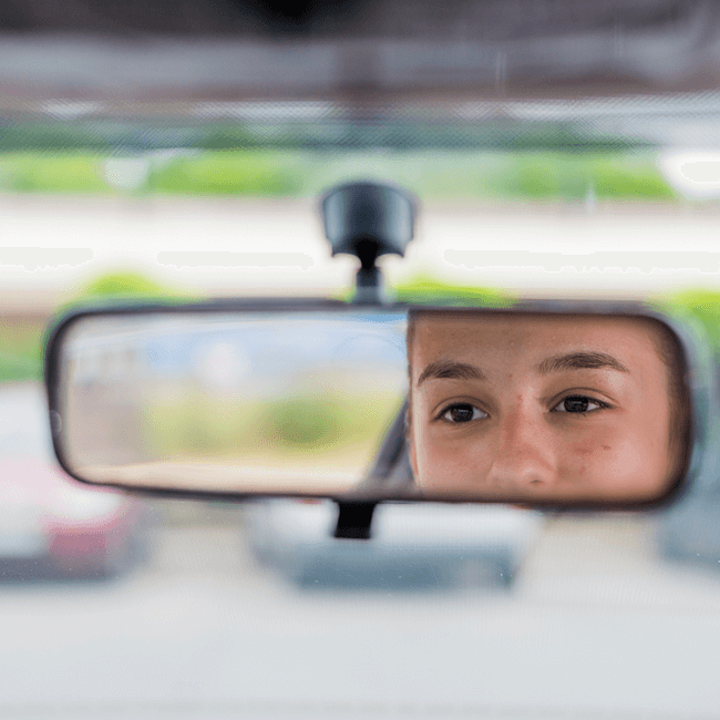 A teen seen through a car rearview mirror