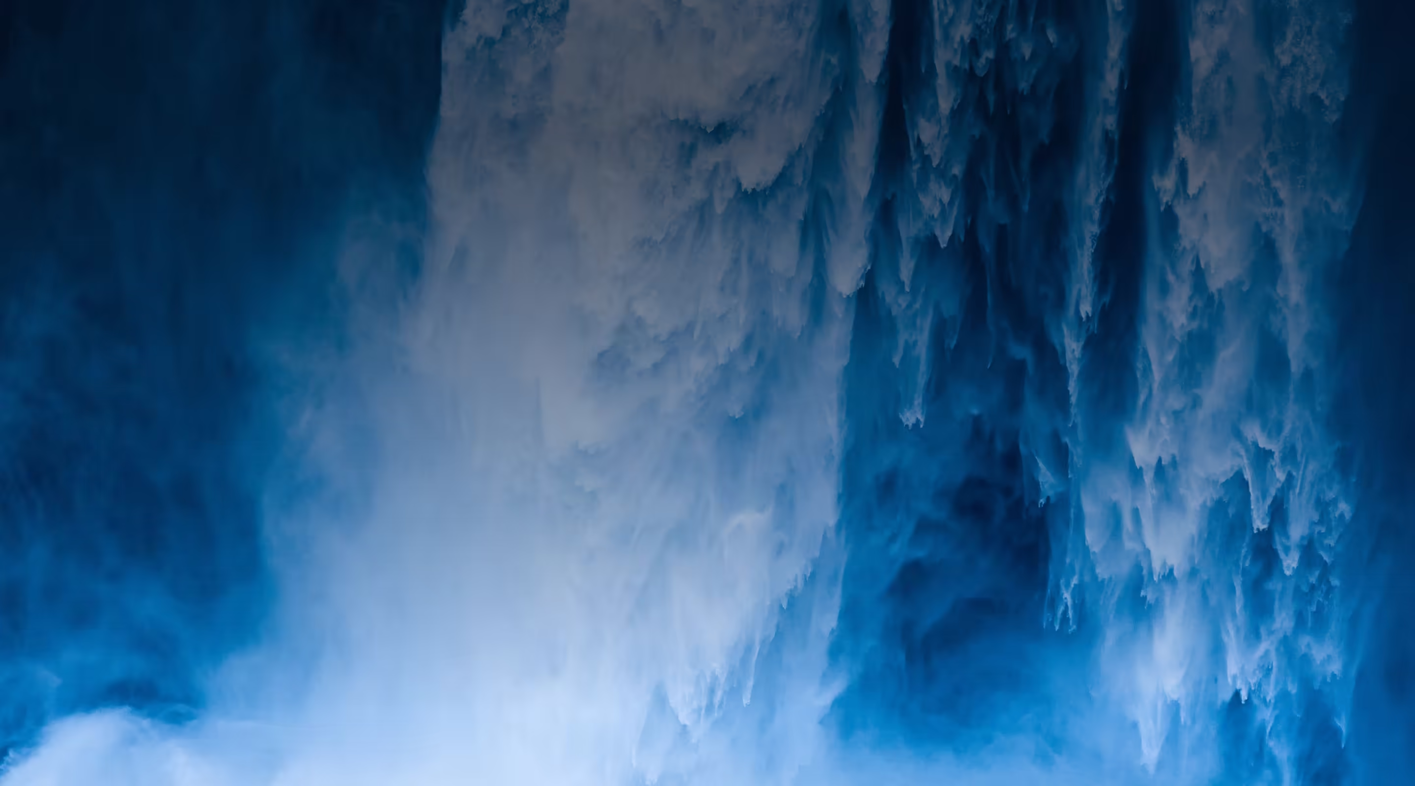 Close-up of powerful water cascading down with white frothy spray and deep blue hues.