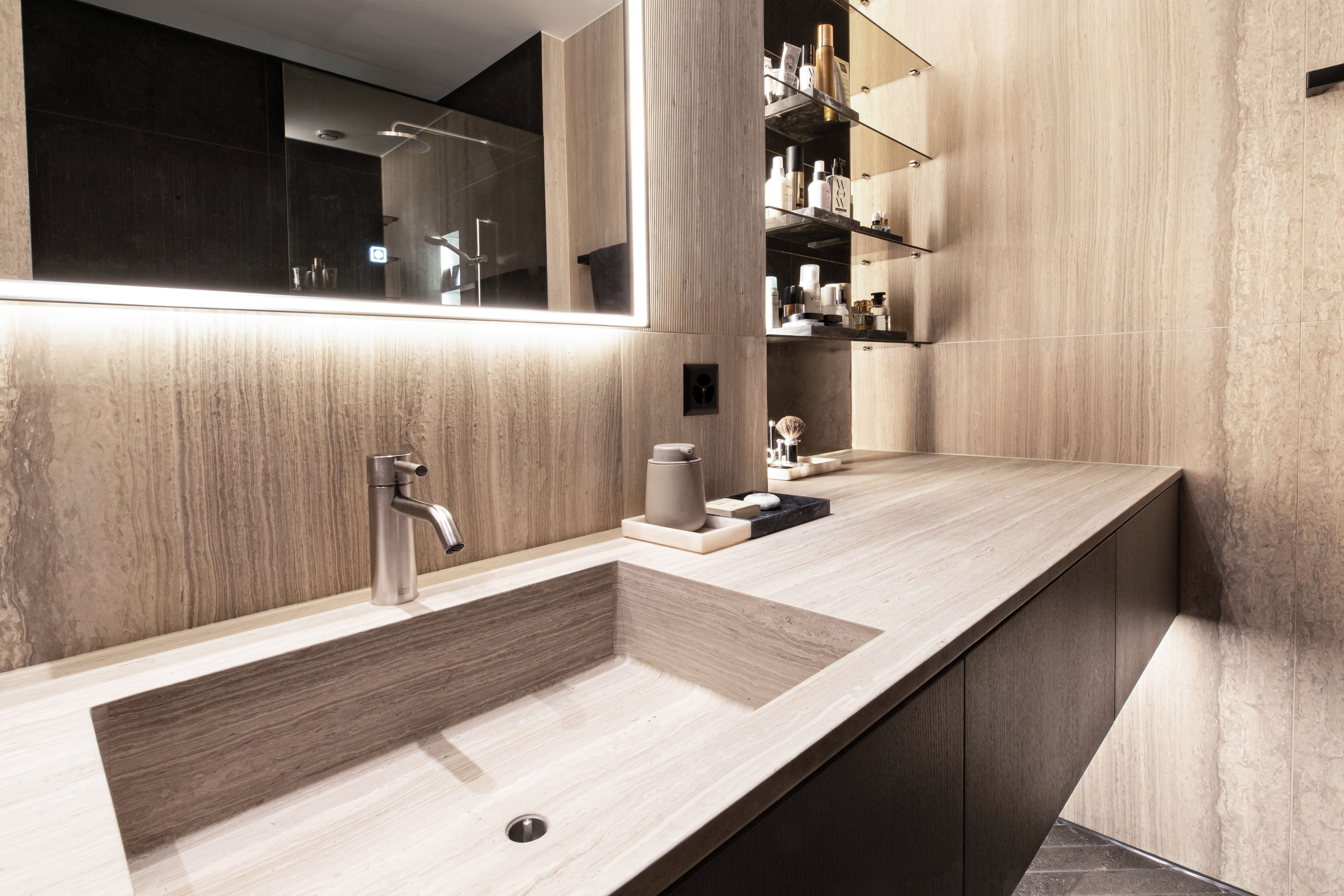 Badezimmer mit Naturstein, Spiegelbeleuchtung und präzise gesetztem Licht