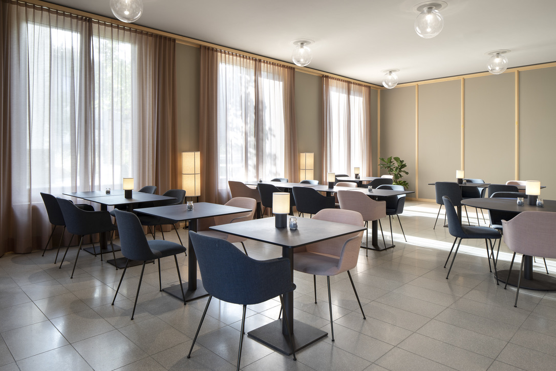 Restaurant Kappi mit dunkelblauen und rosafarbenen Stühlen sowie warmen Lichtinseln auf den Tischen