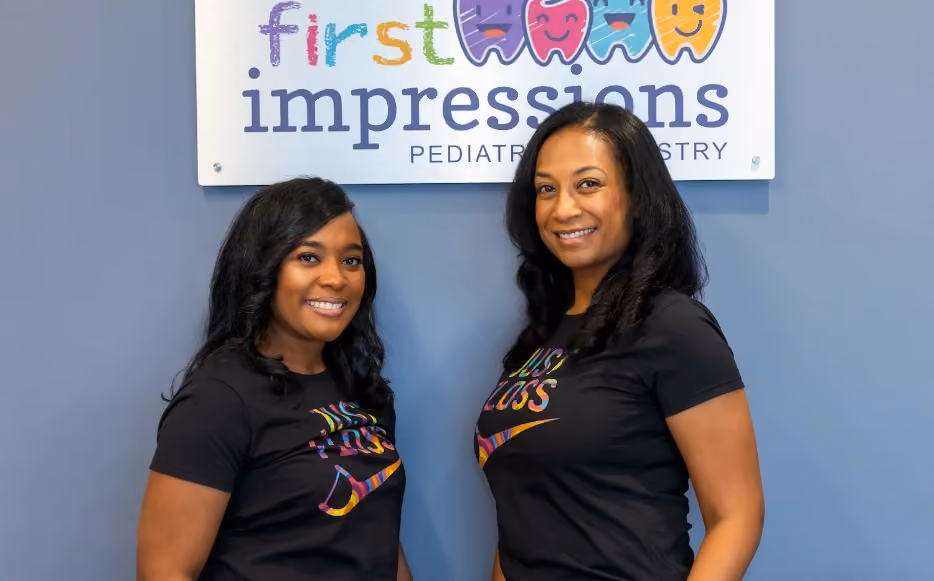 Two First Impressions Pediatric Dentistry team members smiling in front of the practice sign