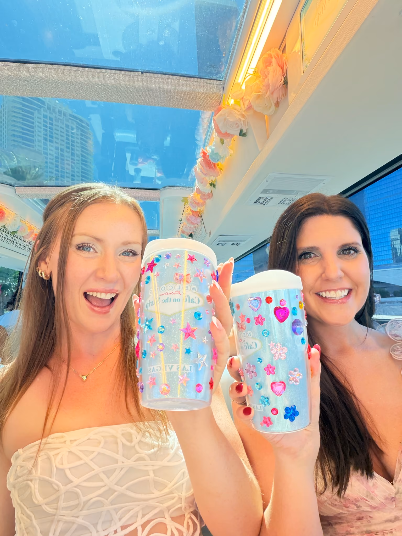 Two guests holding bedazzled Cafe on the Strip tea tumblers aboard the double-decker coach