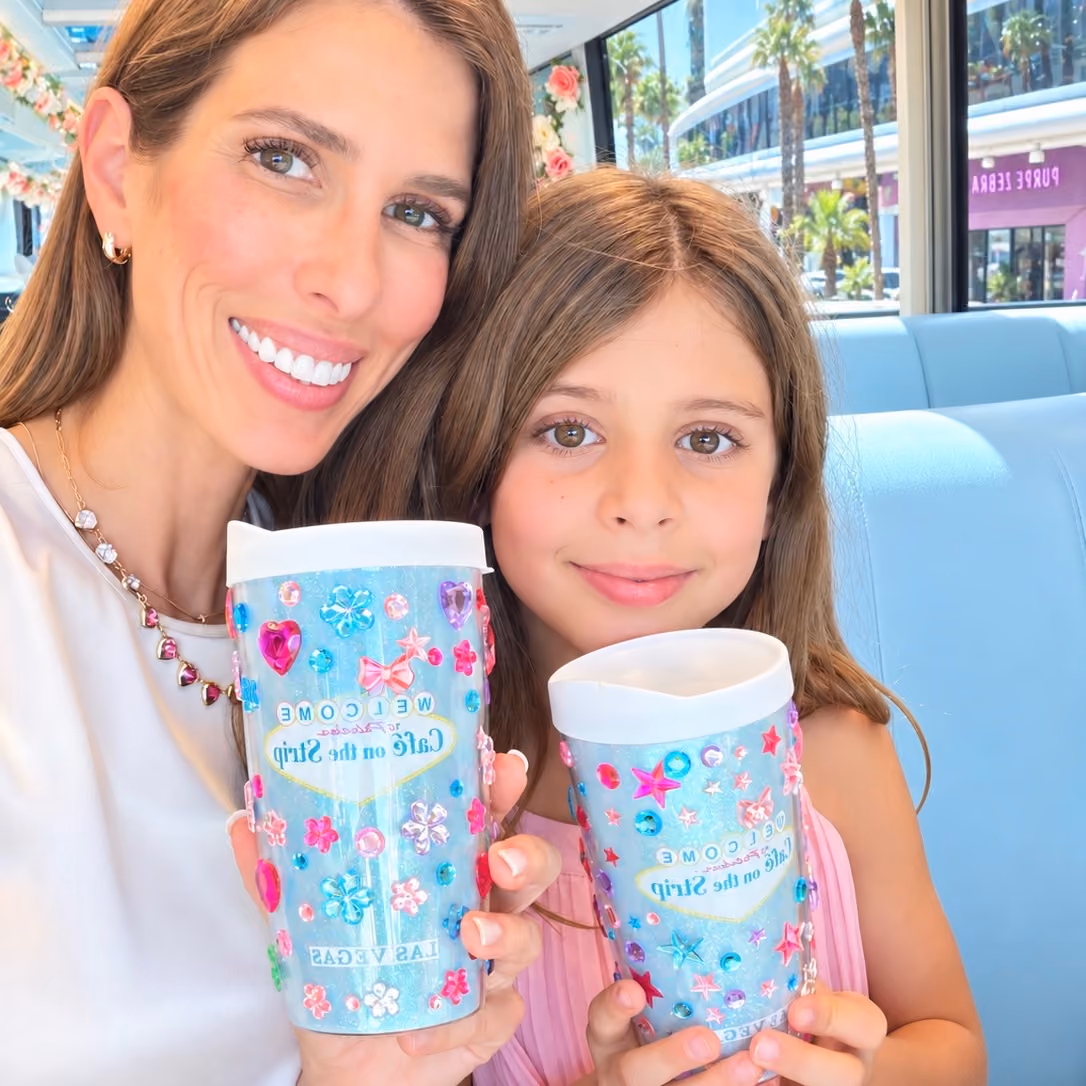 Two girls holding their bedazzled Cafe on the Strip tumblers aboard the coach