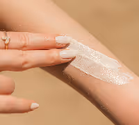 Close-up of a person applying white cream to their forearm with two fingers against a blurred neutral background.