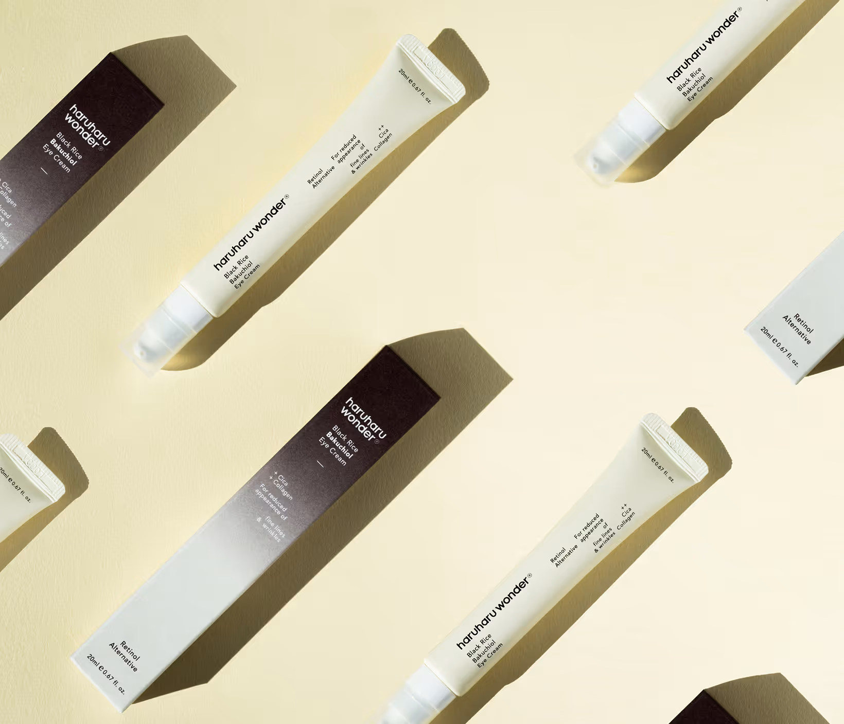 Flat lay of white and black skincare tubes and boxes on a pale yellow background with shadows.