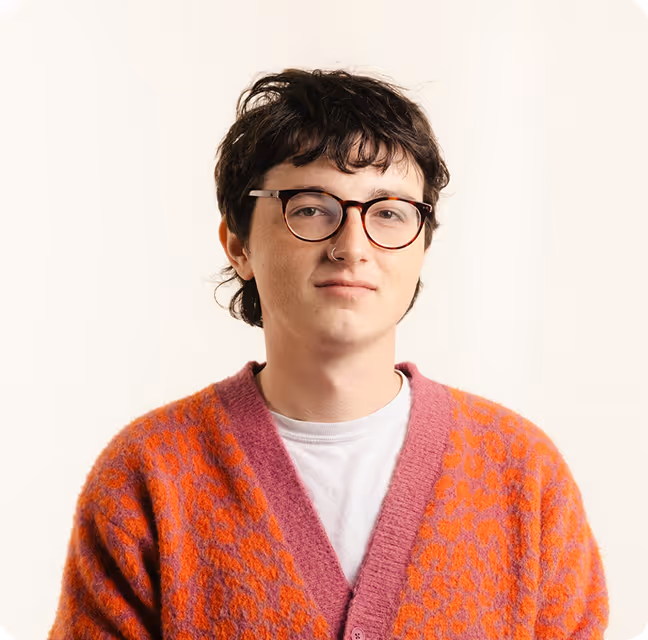 Young person with short dark hair and glasses wearing a white shirt and orange patterned cardigan.