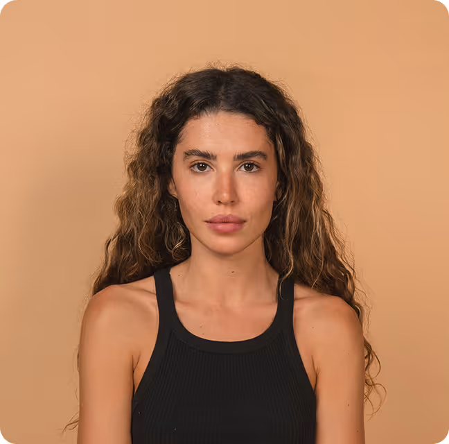 Woman with long curly hair wearing a black sleeveless top against a beige background.