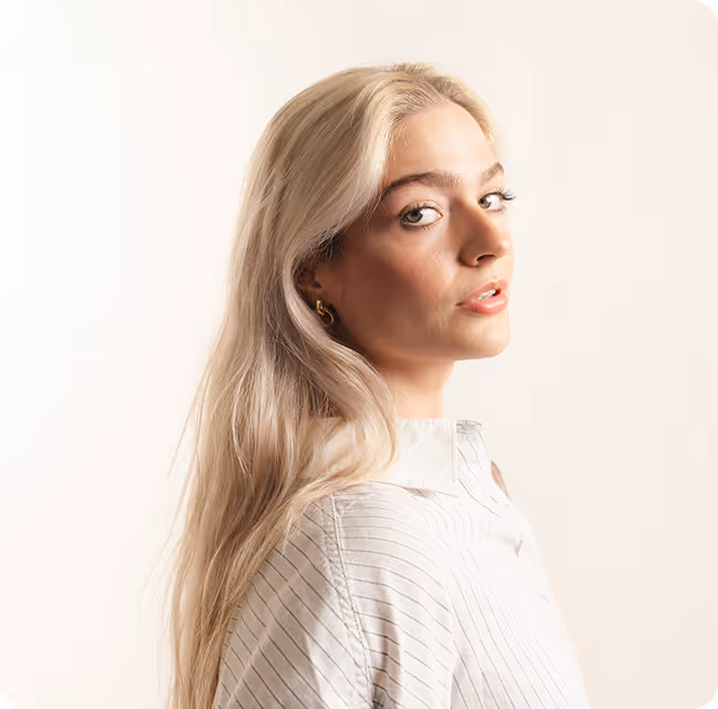 Portrait of a woman with long blonde hair wearing a white striped blouse looking over her shoulder.