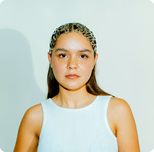 Woman with sleek dark hair held back by multiple black hair clips wearing a white sleeveless top against a light background.