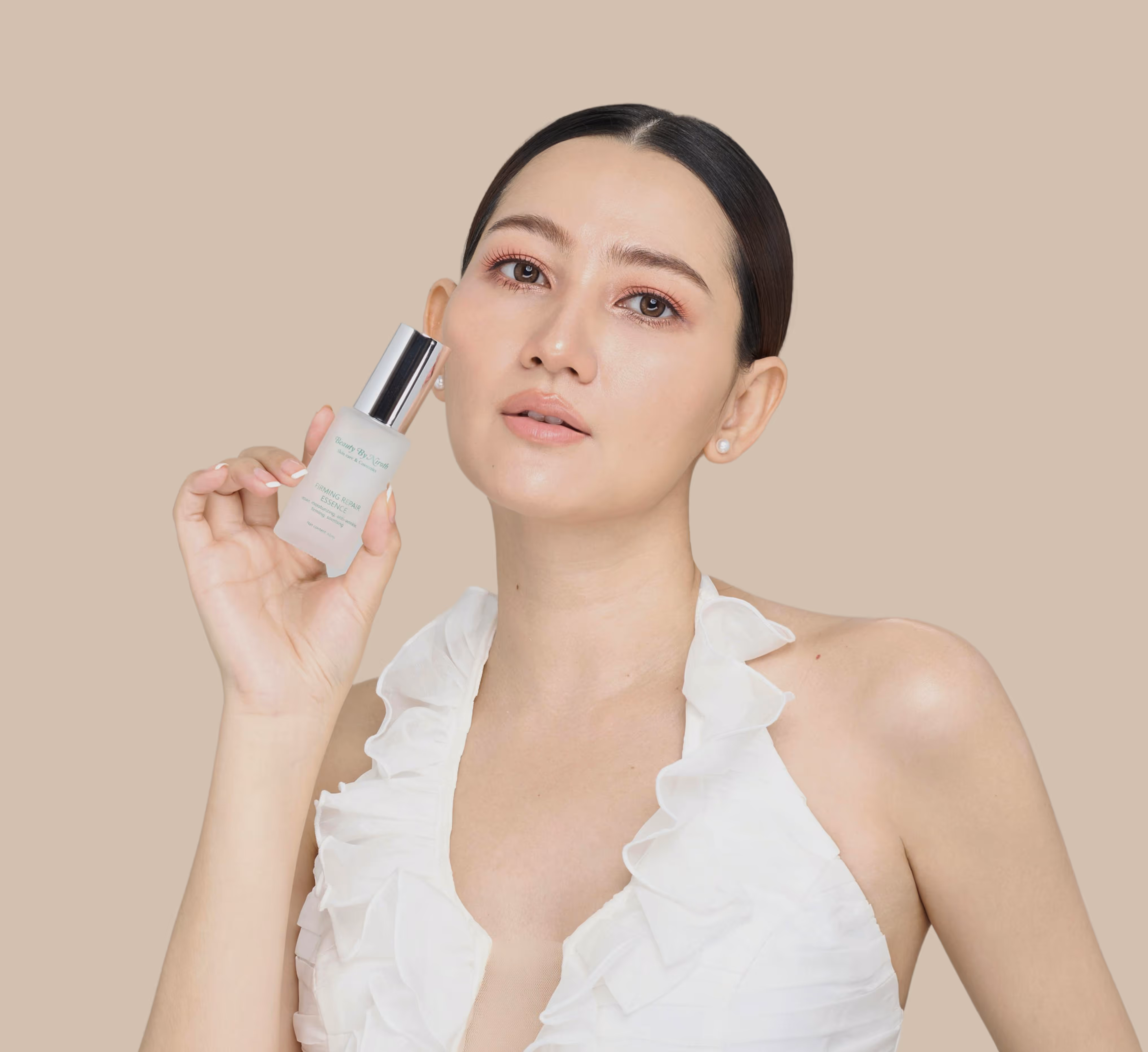 Woman with slicked-back hair in a white ruffled top holding a bottle of firming repair essence skincare product.