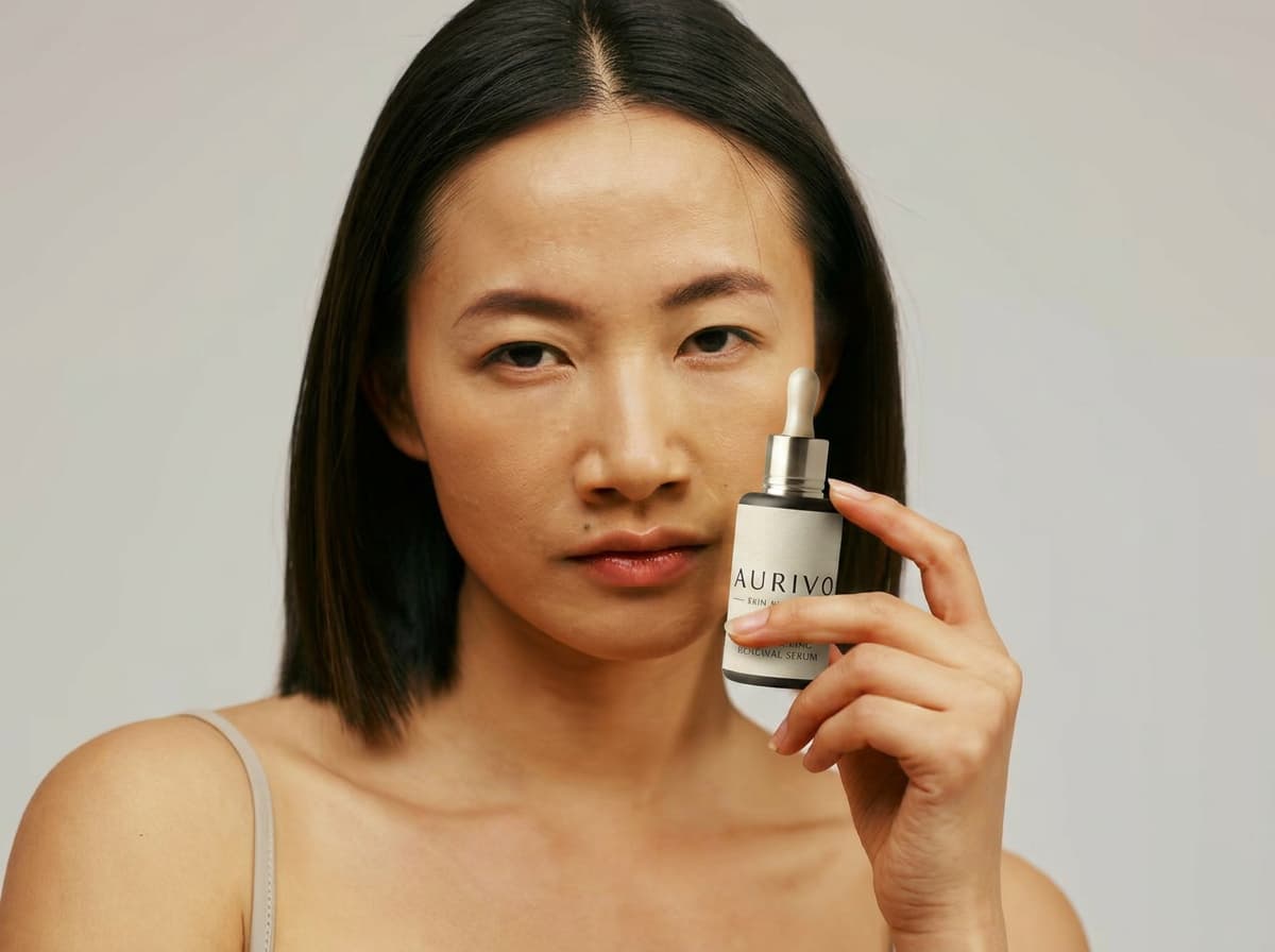 Woman with straight dark hair holding a mint green dropper bottle near her face.