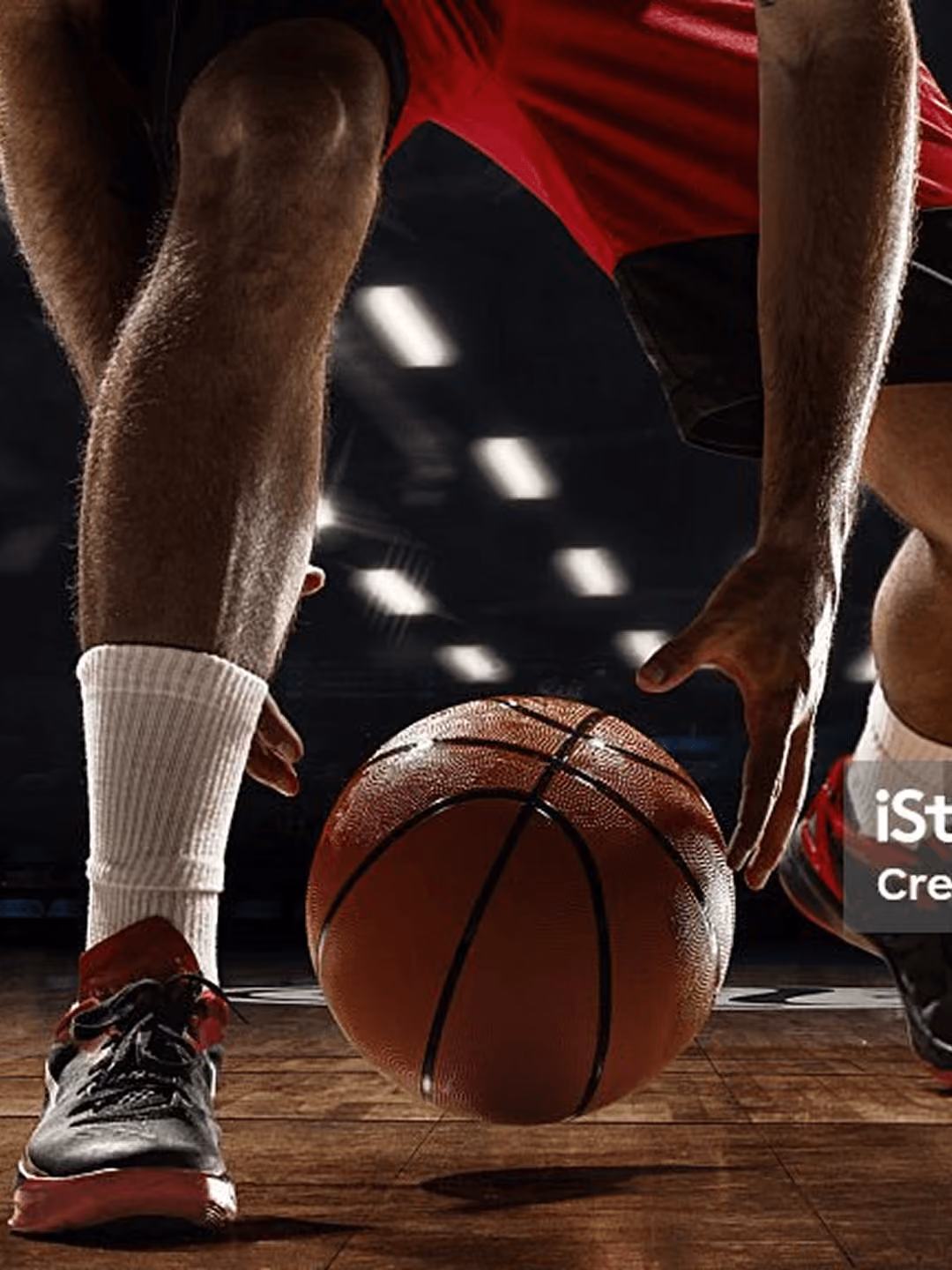 Basketballspieler dribbelt auf Hallenboden, Fokus auf Ball und Beine, rote Shorts, dynamische Bewegung.