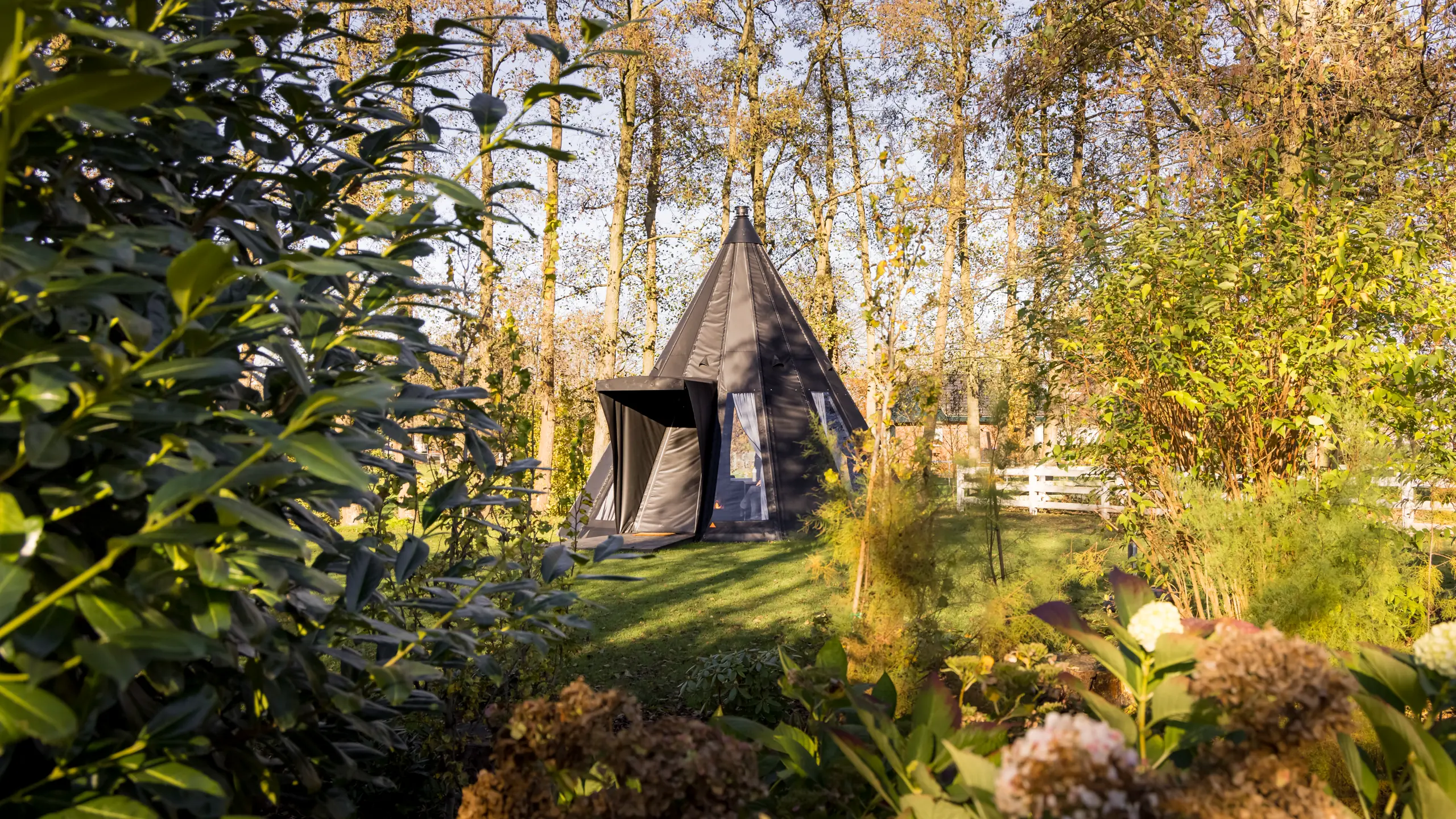 Donkergrijze tipi als vergaderpaviljoen, met de ingang open, op het gras tussen de bomen en struiken van de Blue Bricks campus