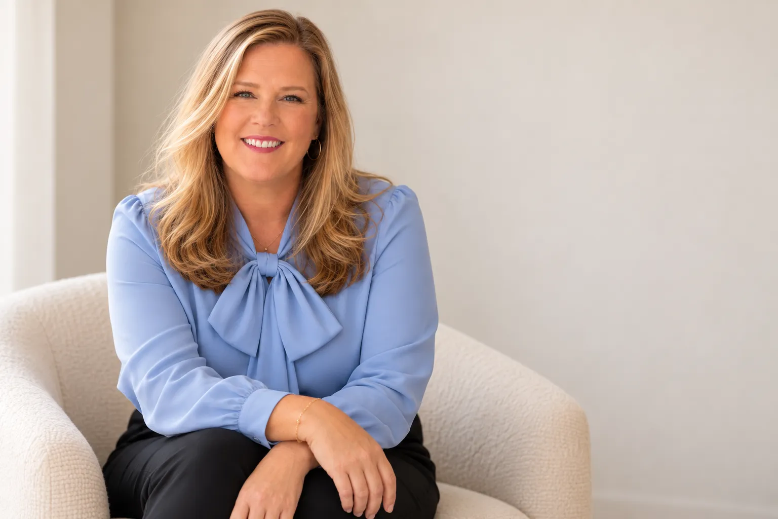 Polly Keene seated in a cream boucle chair, wearing a periwinkle blue bow blouse