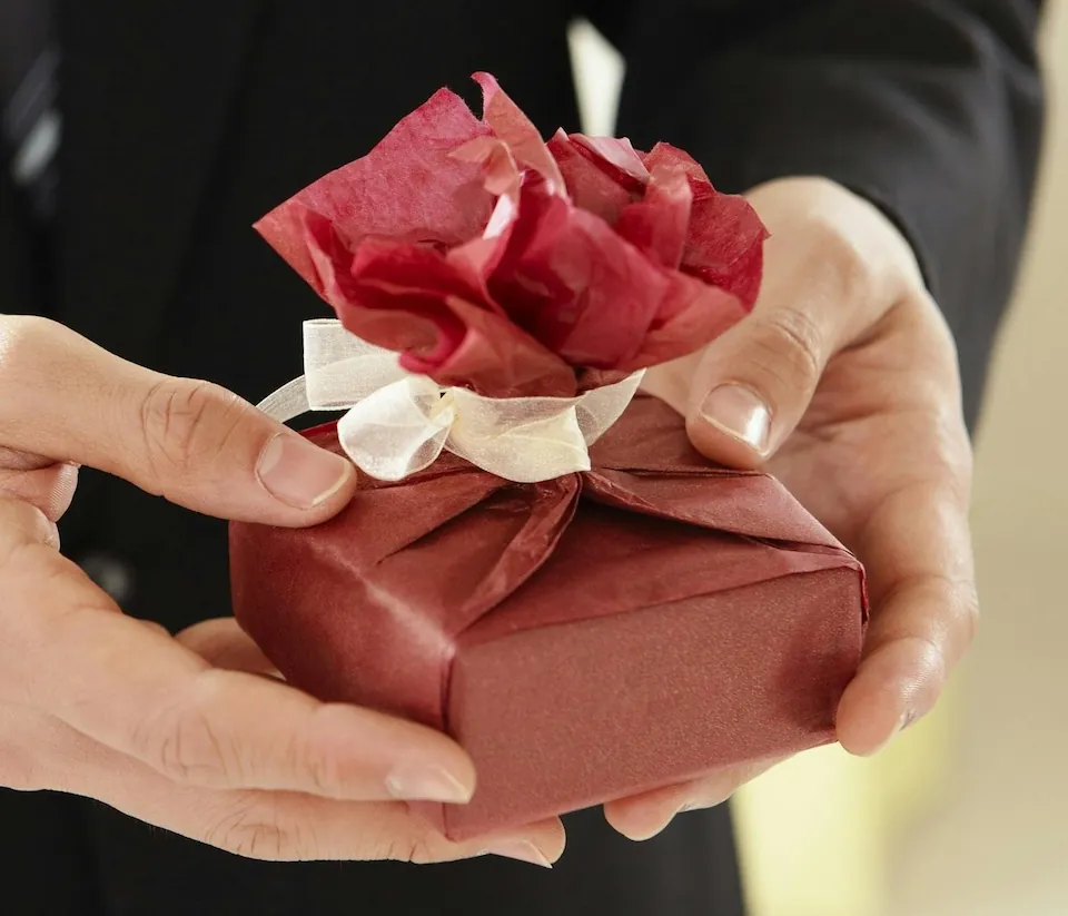 Hands holding a small gift wrapped in red wrapping paper