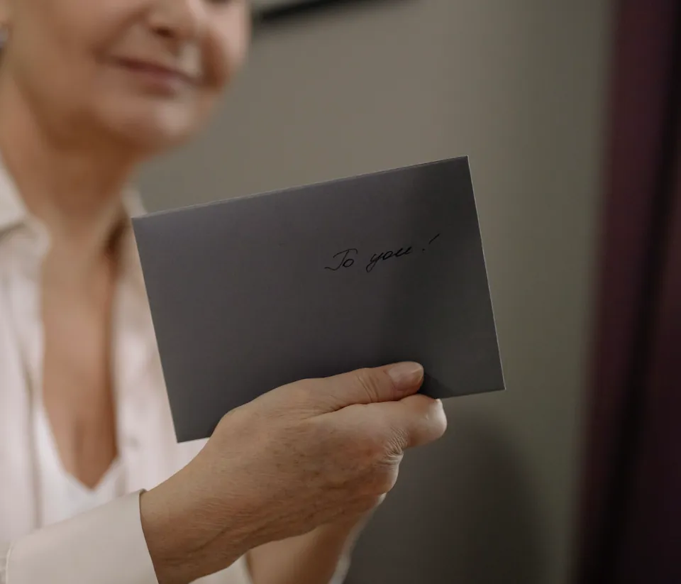 Woman holding a charcoal gift envelope inscribed "to you" for a Giftada membership gift