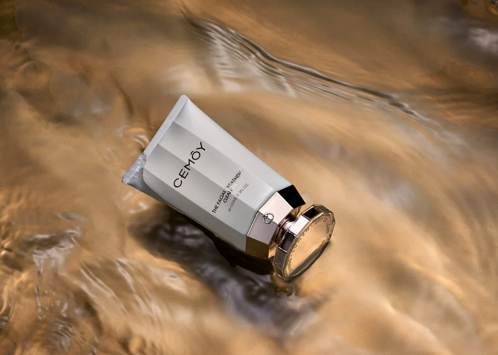 Tube of Cemoy facial treatment cleanser lying on rippling golden water surface.