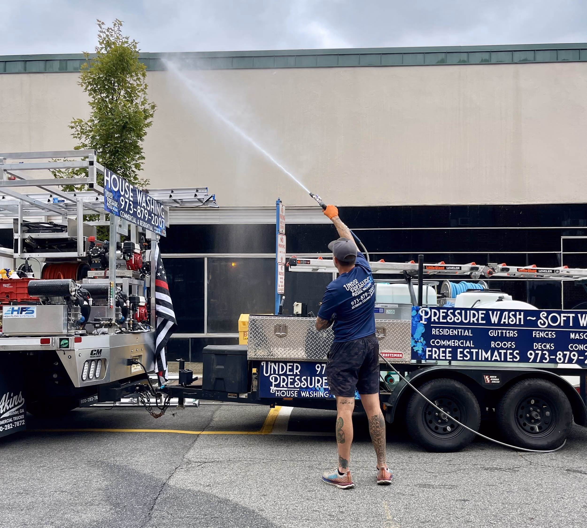 Man using a pressure washer to clean a building exterior from a truck with cleaning equipment.
