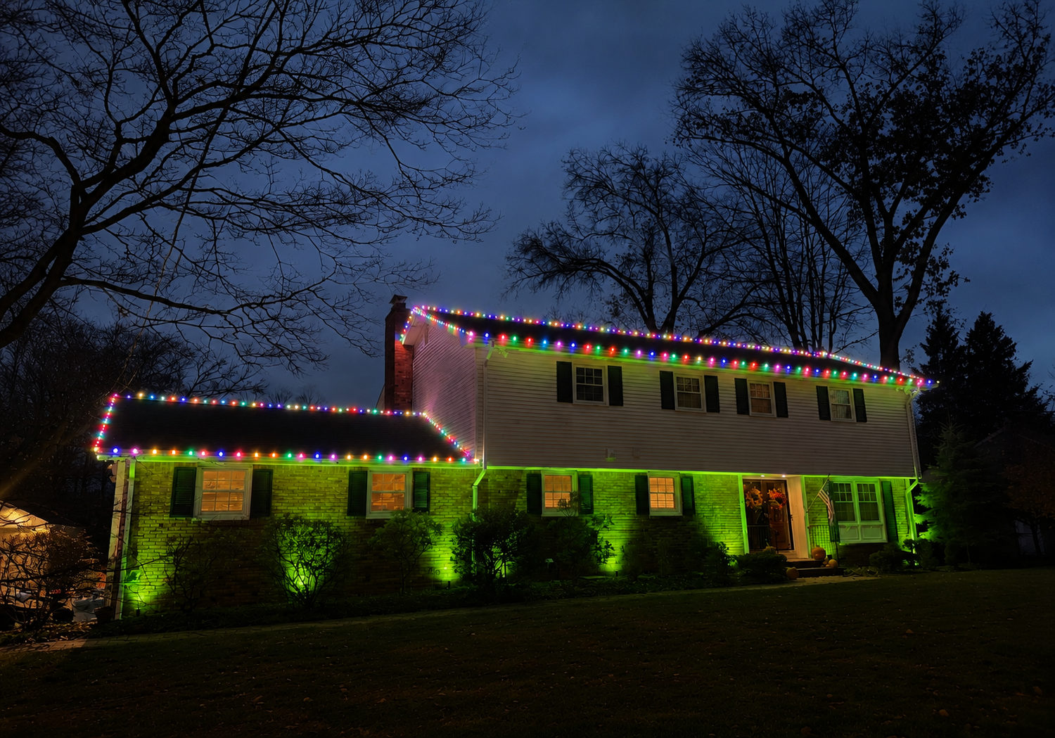 Multicolor C9 Christmas lights installed along the rooflines of a New Jersey home with landscape uplighting