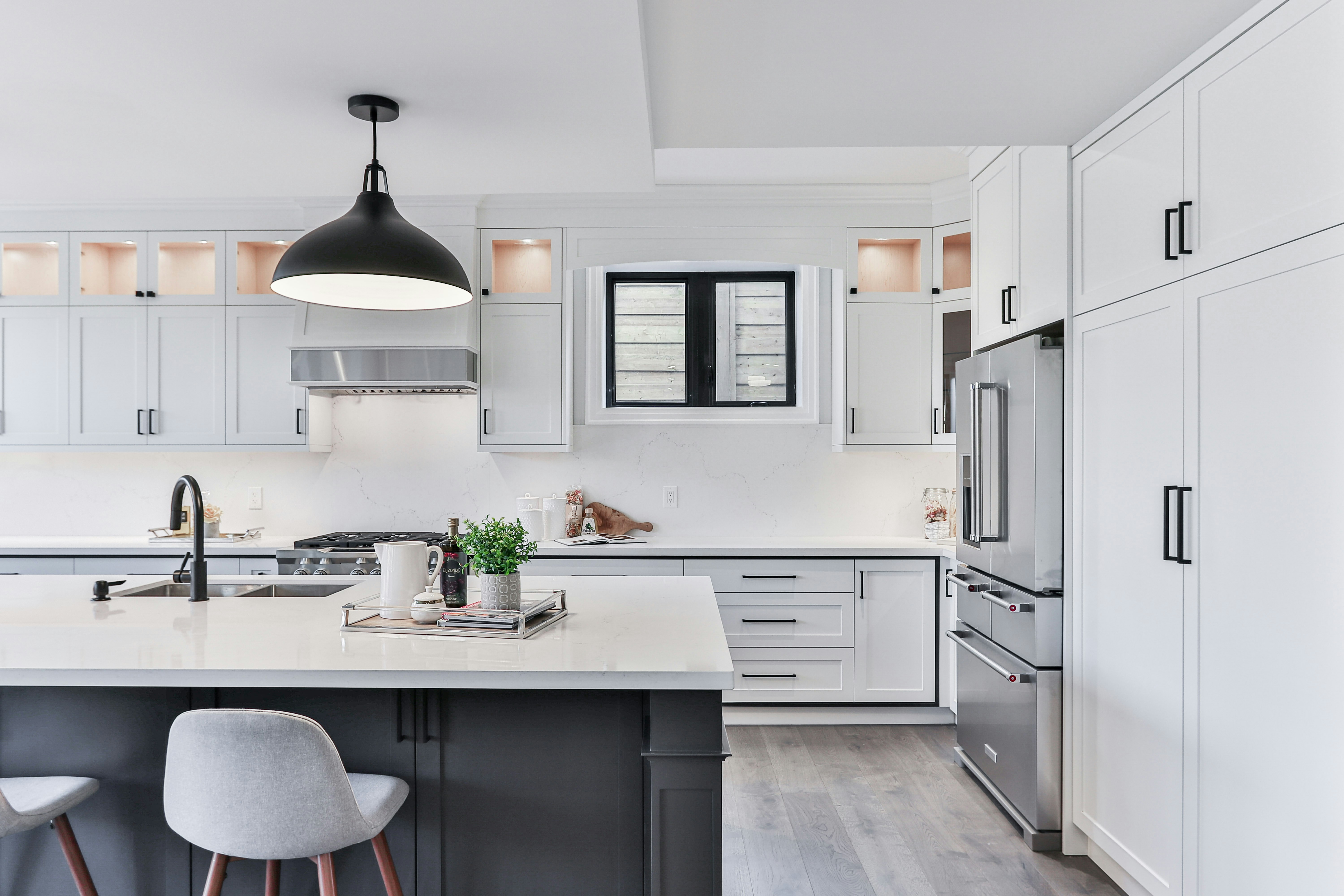 Modern kitchen with white cabinets, black island, gray chairs, and stainless steel refrigerator.