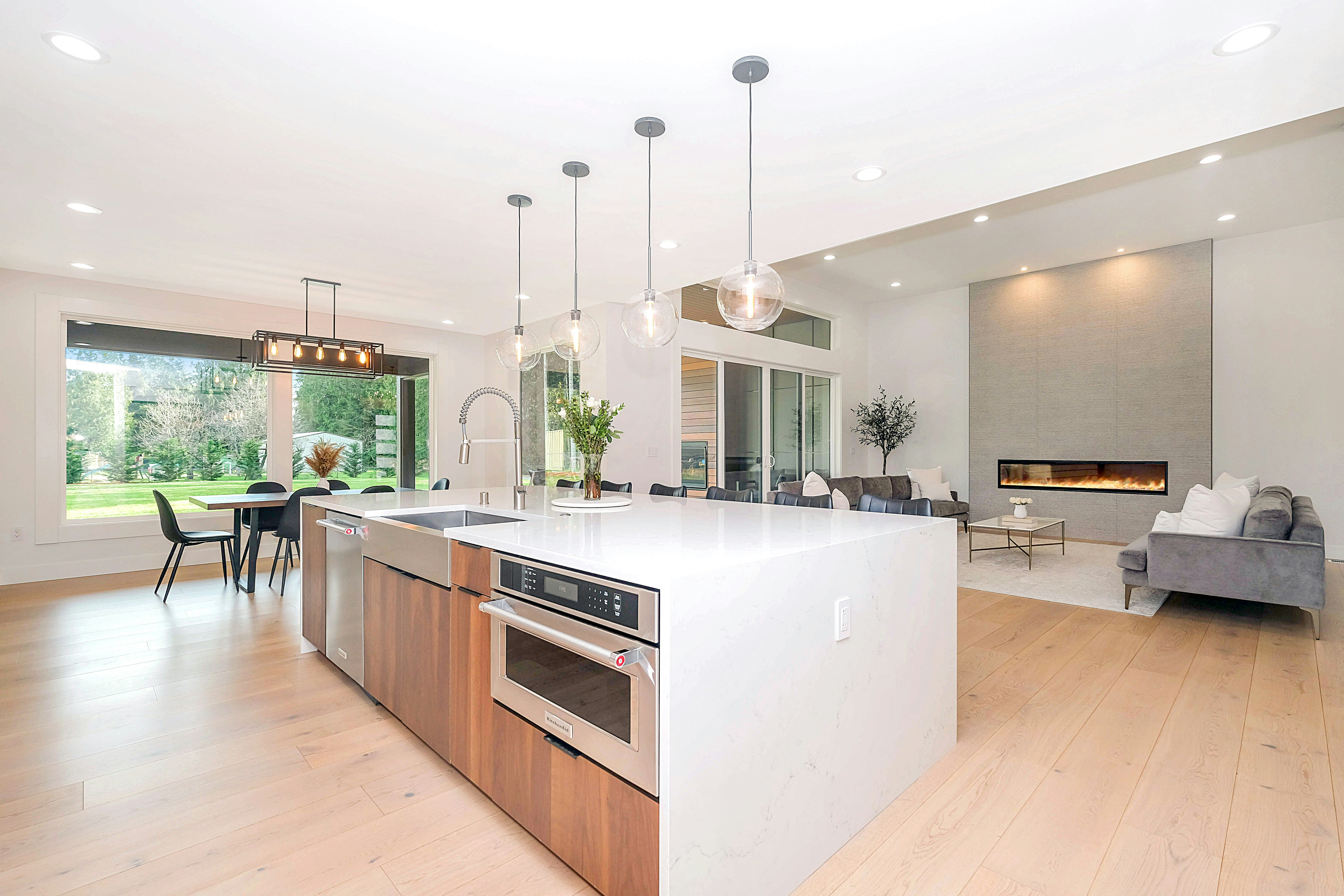 Modern open kitchen with a large white marble island, wooden cabinets, and glass pendant lights.