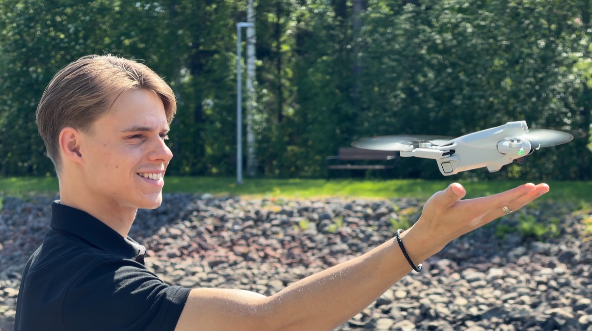 Nuori mies hymyilee pitelemällä pienoisdronen ilmassa avoimella kädellä ulkona.