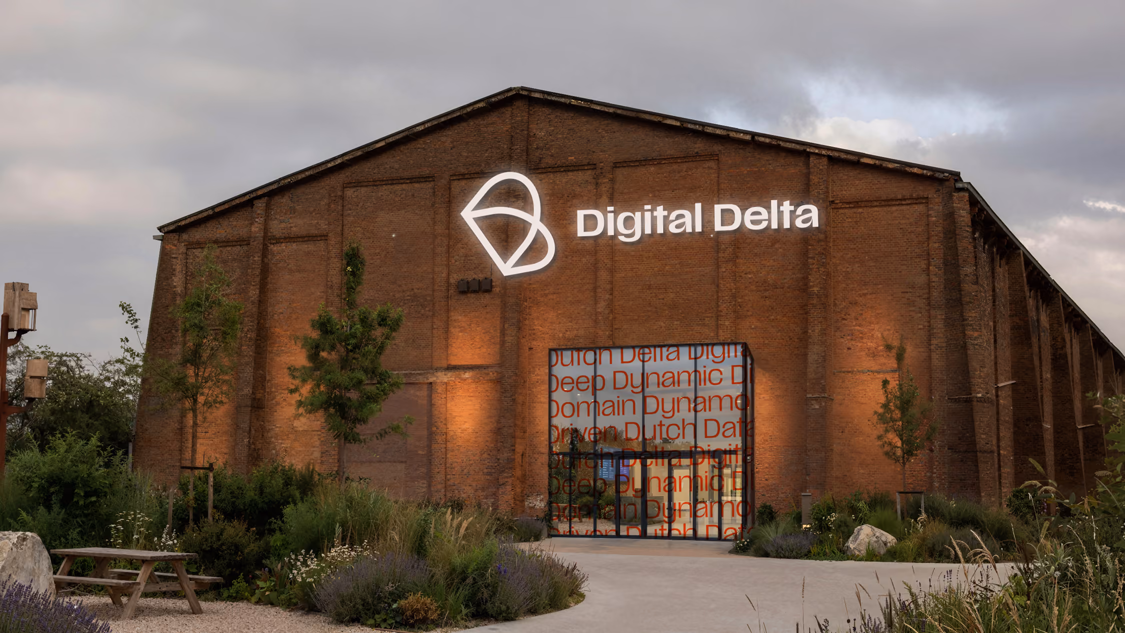 Bakstenen industrieel gebouw met 'Digital Delta' logo en planten, banken buiten.