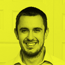 Smiling man with short dark hair and beard against a yellow background.
