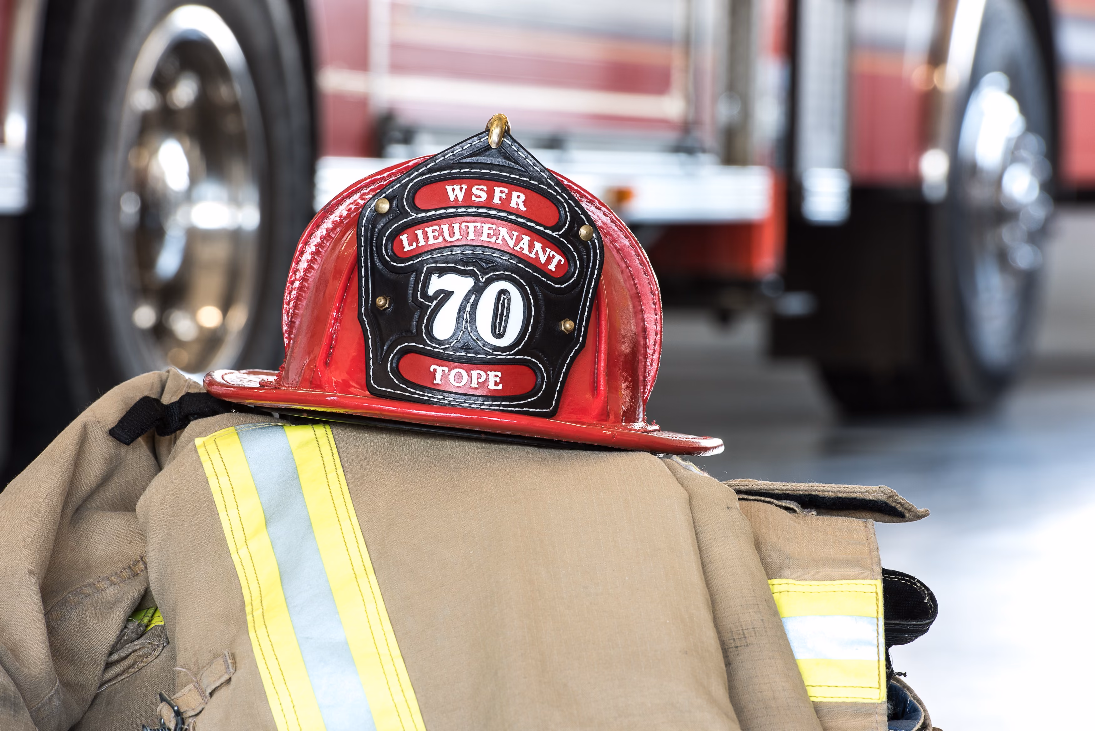 Firefighter's red helmet labeled Lieutenant 70 rests on tan turnout gear with reflective stripes.