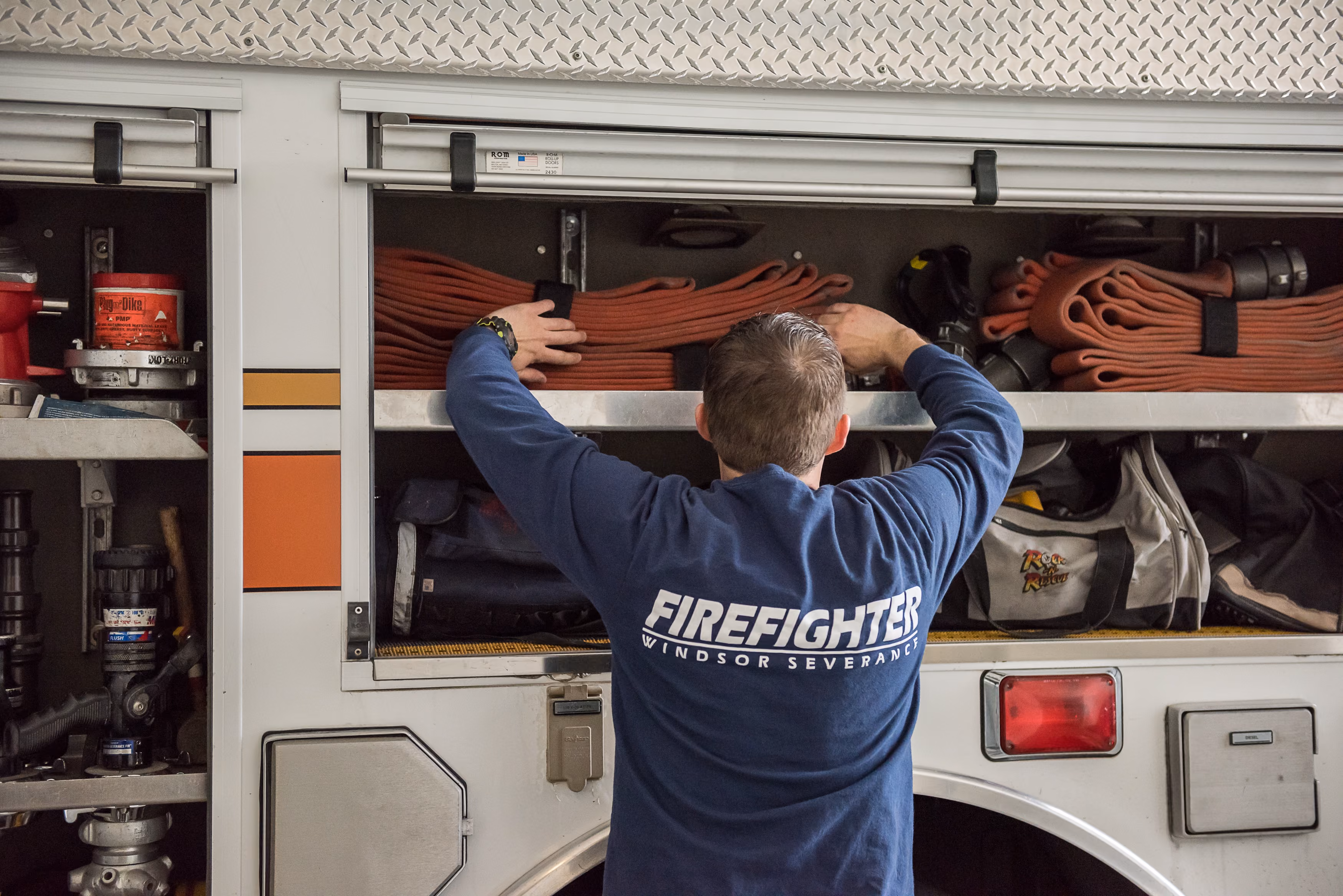 Firefighter arranging fire hoses in a compartment of a fire truck labeled Windsor Severance.