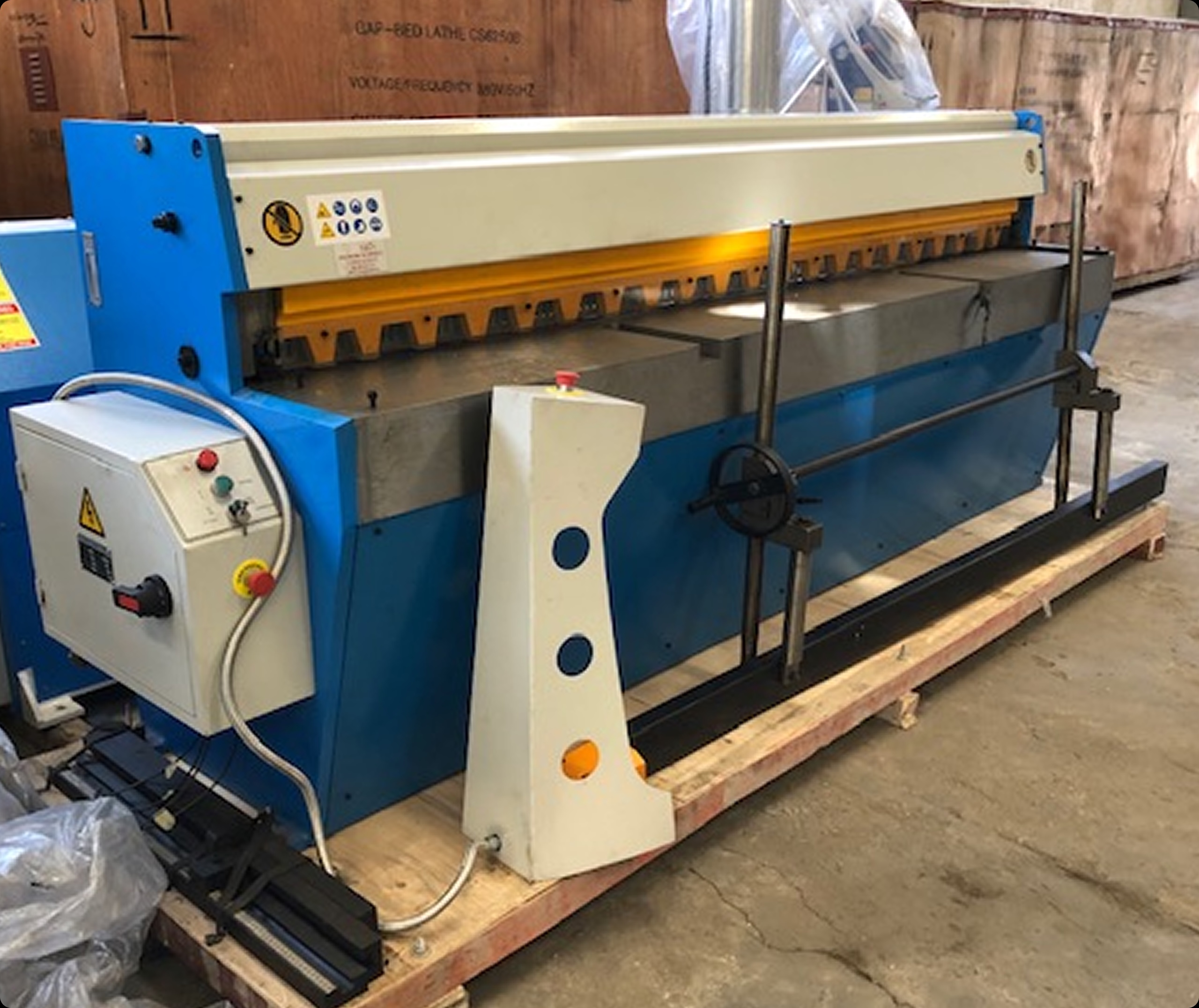 Industrial blue and beige sheet metal bending machine on wooden pallet in warehouse.