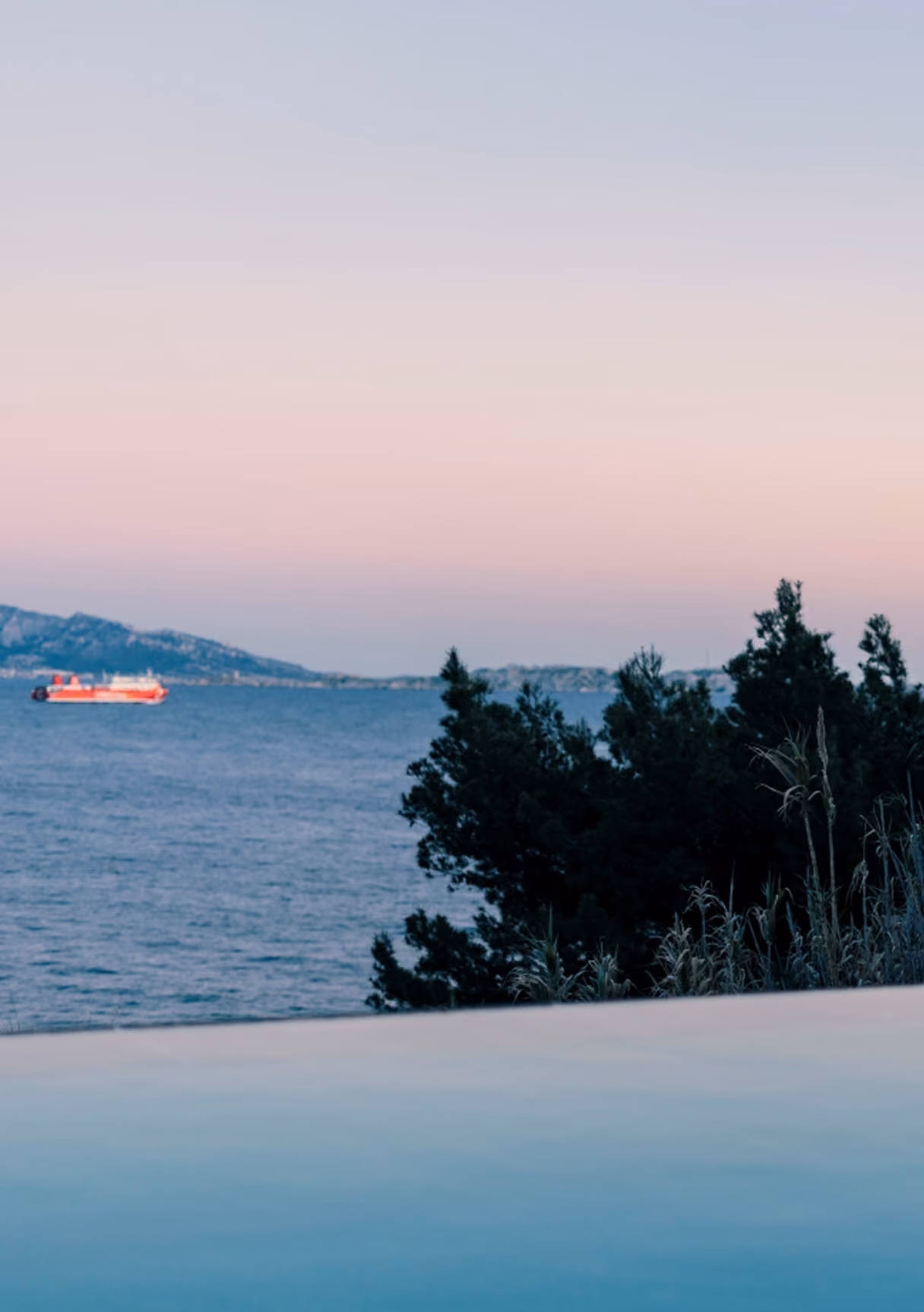Vue paisible sur la mer avec un bateau rouge et des arbres au coucher du soleil.