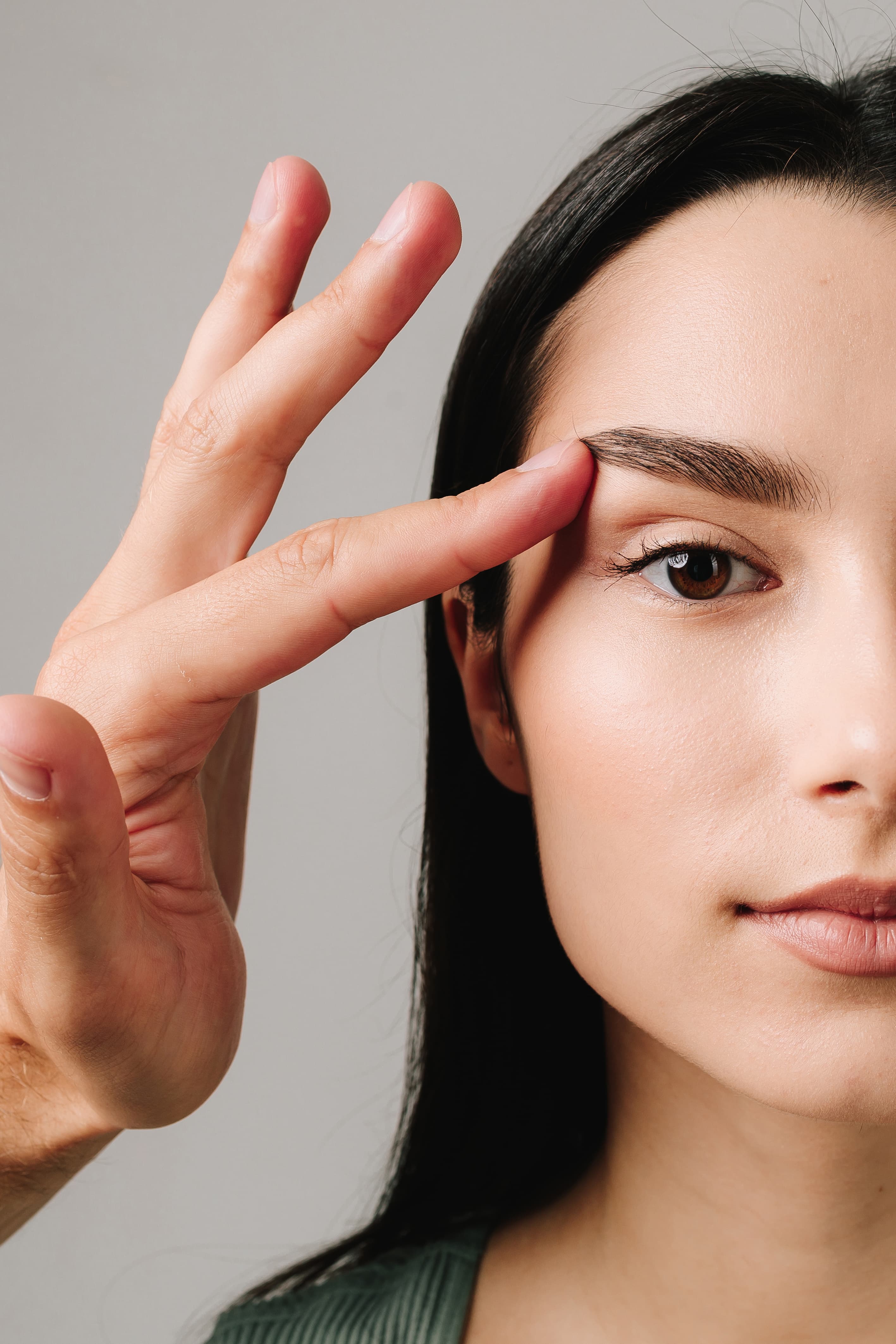 Hand shaping or grooming the eyebrow of a woman with clear skin and dark hair.