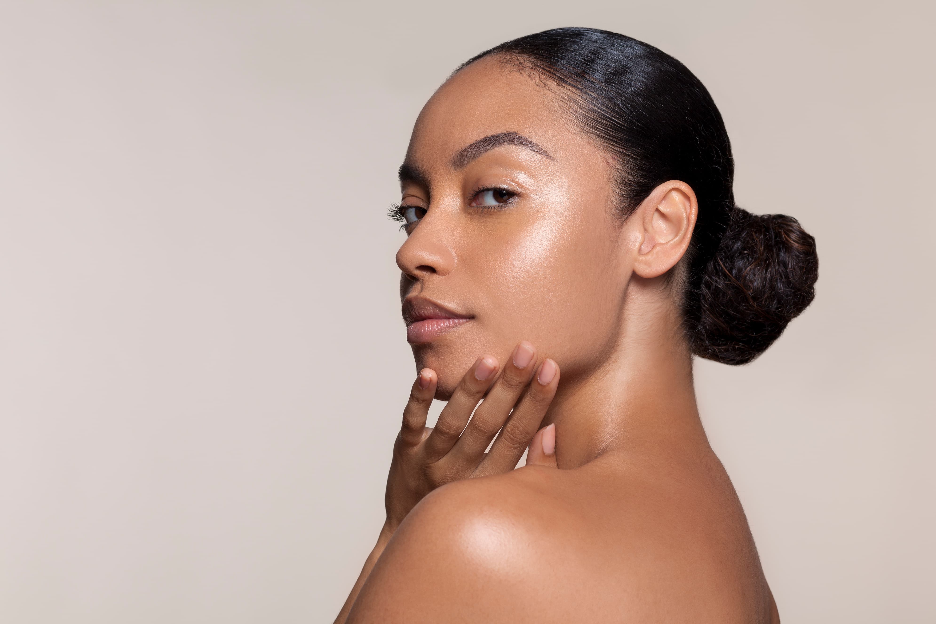 Side view of a woman with smooth skin and hair in a bun, gently touching her chin.