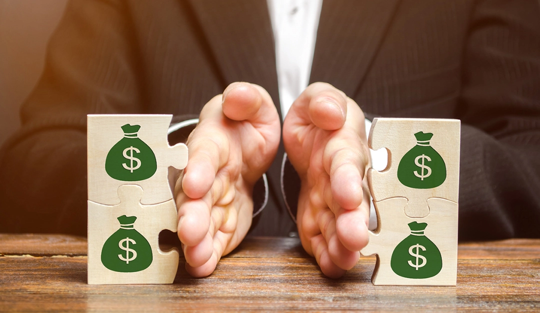 Hands separating two pairs of wooden puzzle pieces printed with green dollar money bags