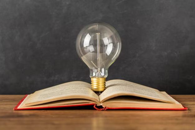 Vintage light bulb standing on an open book with a red cover, against a dark chalkboard background