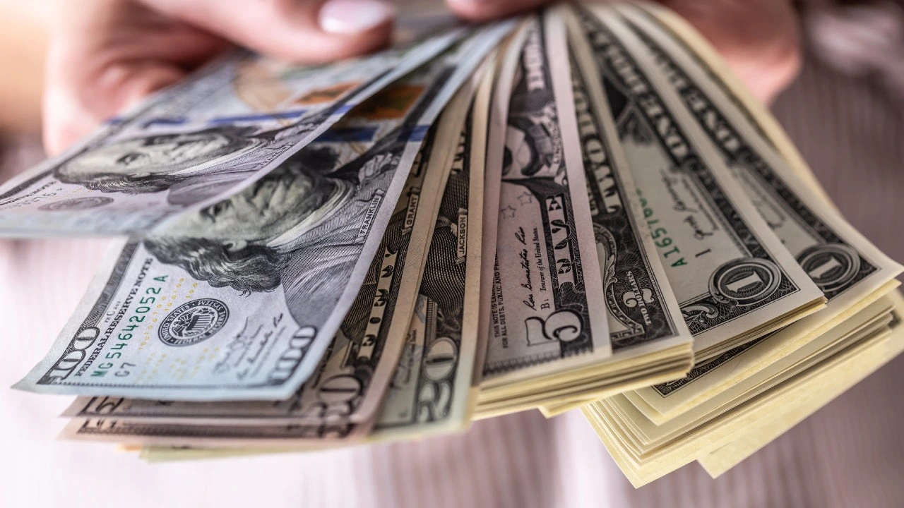 Hands fanning out a wad of US dollar bills of various denominations, from 1 to 100 dollars