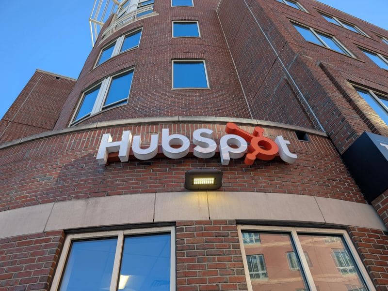 Exterior view of a red brick building with several windows and the HubSpot sign featuring the company name and orange sprocket logo mounted above a light fixture.