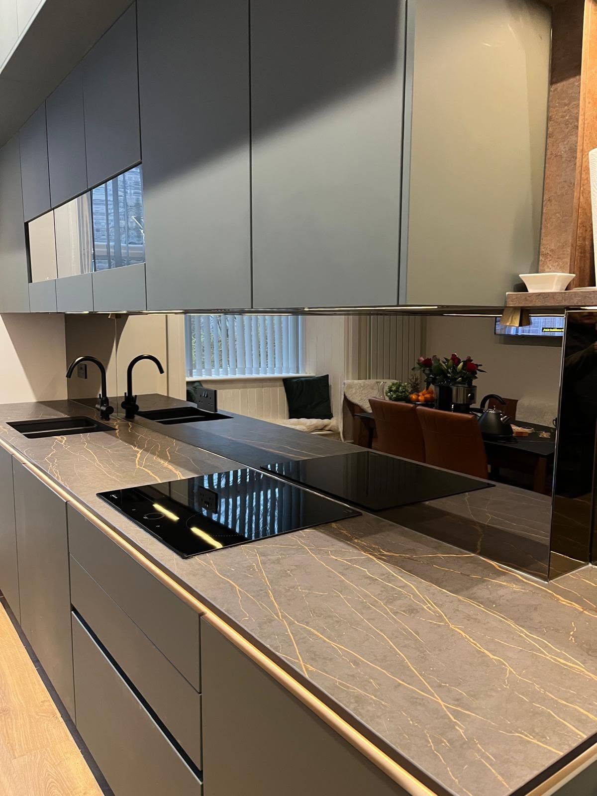 Mirrored glass splashback in a grey modern kitchen reflecting the dining area