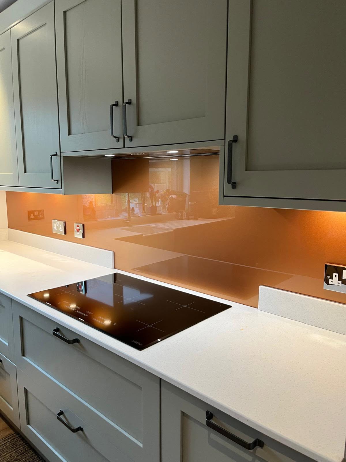 Bronze glass splashback behind a black induction hob in a sage green kitchen