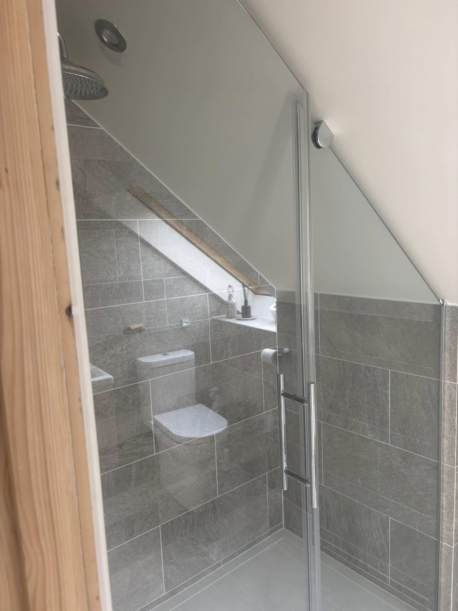 Custom shaped glass shower screen fitted into a sloped loft ceiling bathroom