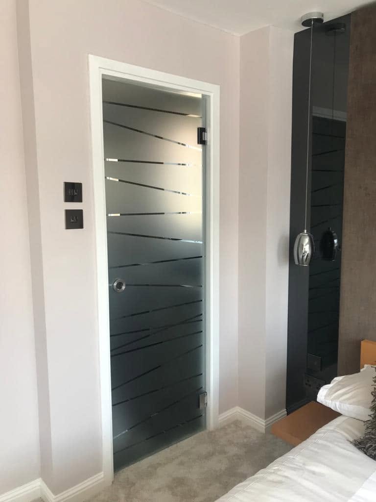 Frameless glass door with sandblasted diagonal stripe pattern in a bedroom