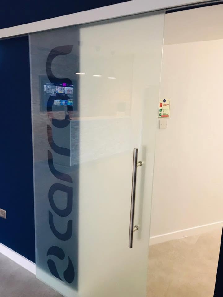 Frameless sliding glass door with branded frosted logo panel, office interior