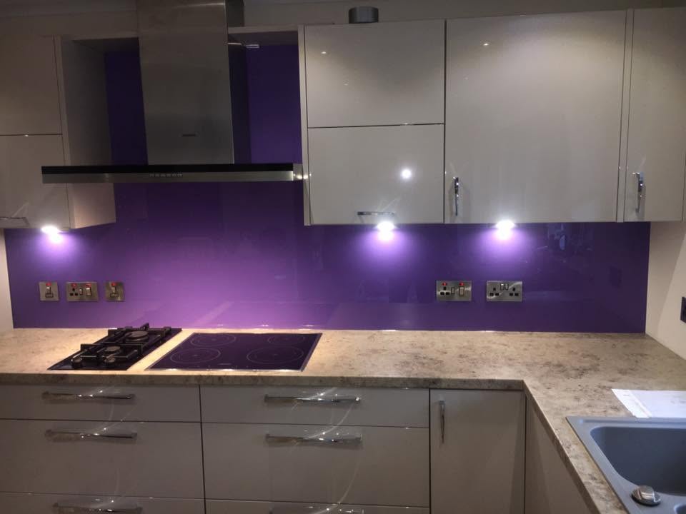 Vivid purple glass splashback behind a gas hob and induction hob in a cream kitchen